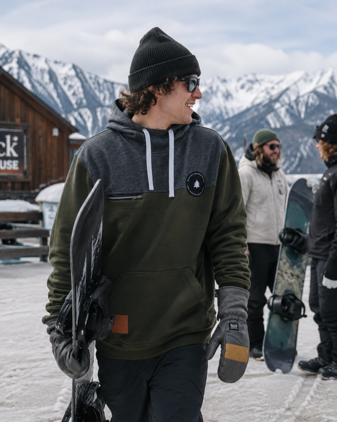 Rider carrying a snowboard in the olive fleece tall hoodie